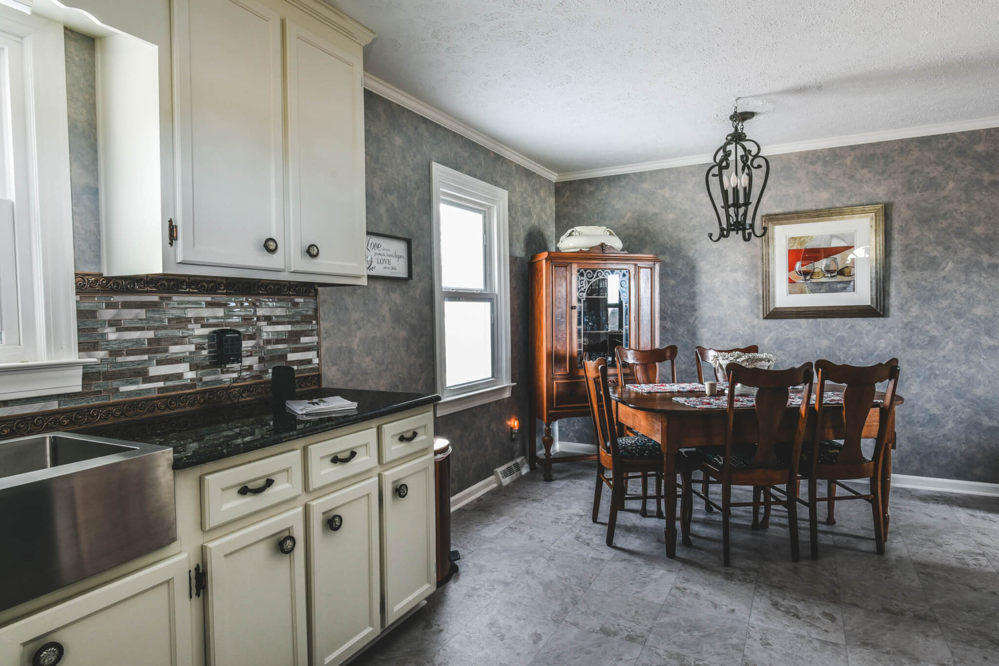 A kitchen and dining area with a table and chairs, white cabinets, a dark countertop, and wall decor.