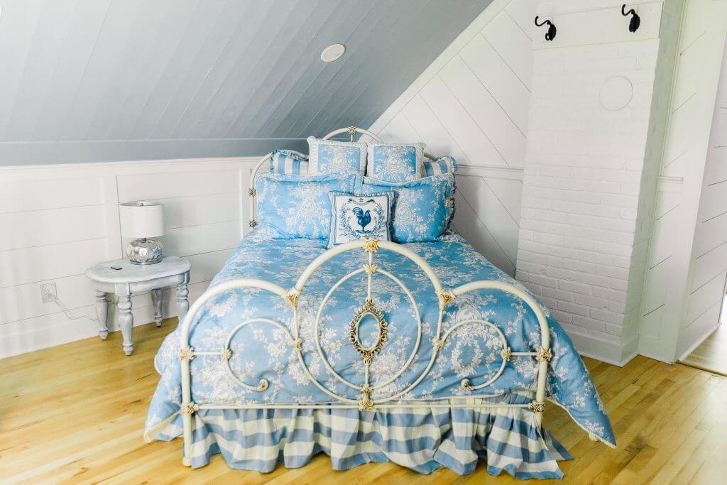 experience oakhaven venues in greensboro 4 A neatly arranged bedroom with a metal-framed bed covered in blue and white patterned linens, a round side table with a lamp, and a white brick accent wall.