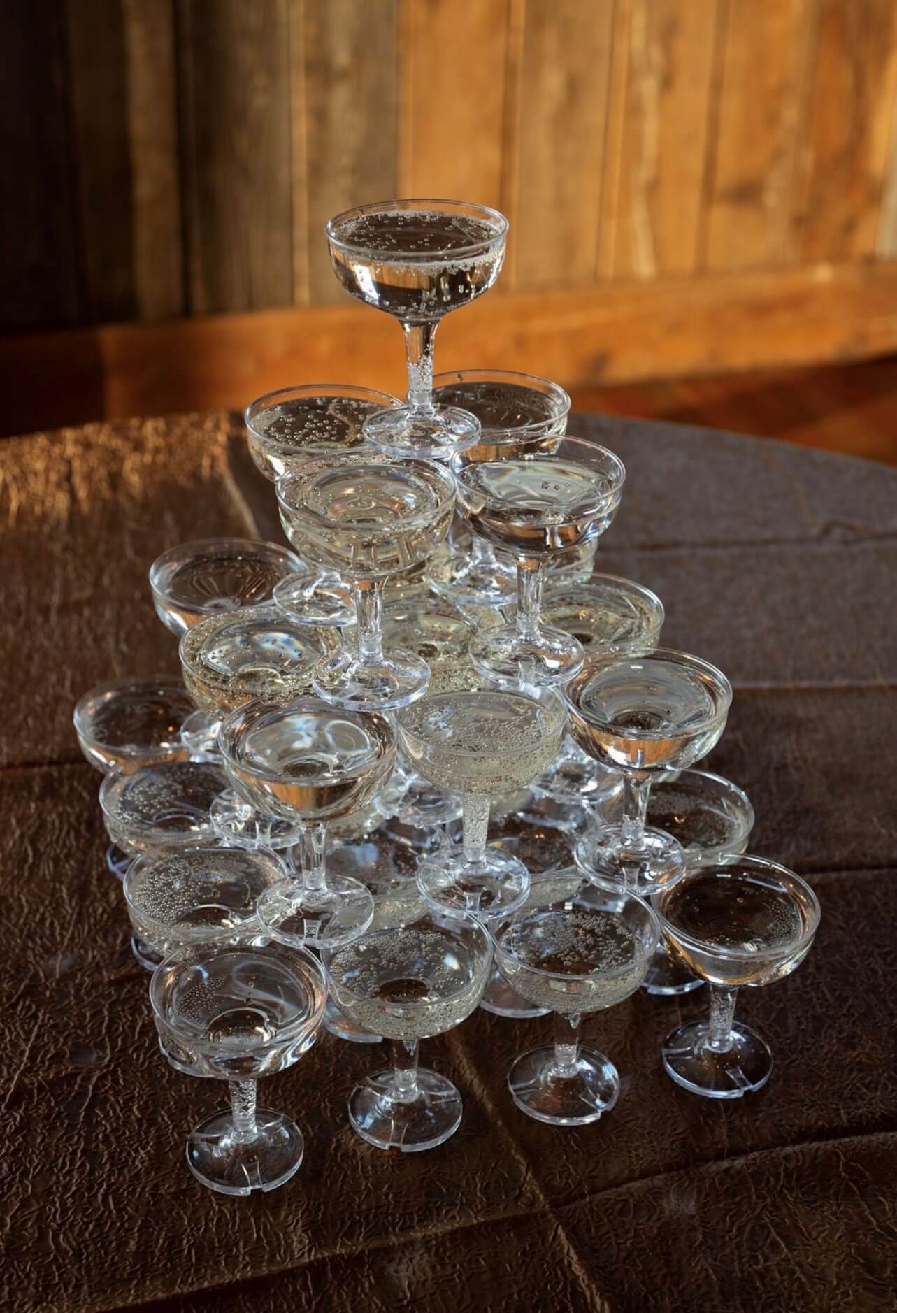 A champagne tower made of filled coupe glasses is arranged on a wooden table.