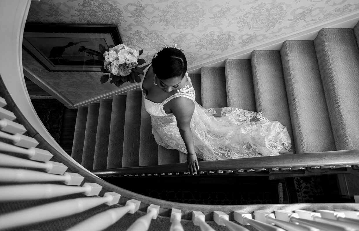 experience oakhaven wedding venue north carolina 21 Bride in a lace gown ascends a carpeted staircase, holding a bouquet, with one hand on the railing.