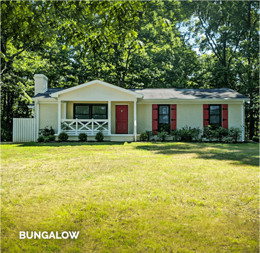 Single-story bungalow with white siding, red shutters, and a red door, surrounded by grass and trees.