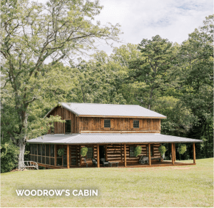 A rustic log cabin with a metal roof surrounded by lush trees and green grass, with a sign reading "Woodrow's Cabin" at the bottom left.