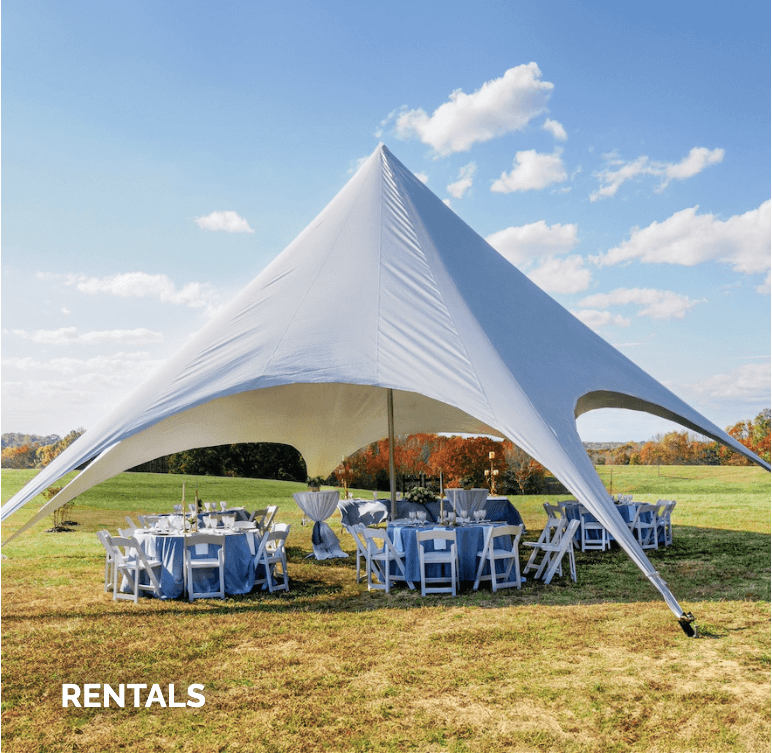 Large white tent on grassy field with tables and chairs set up underneath. Blue skies and clouds in the background.