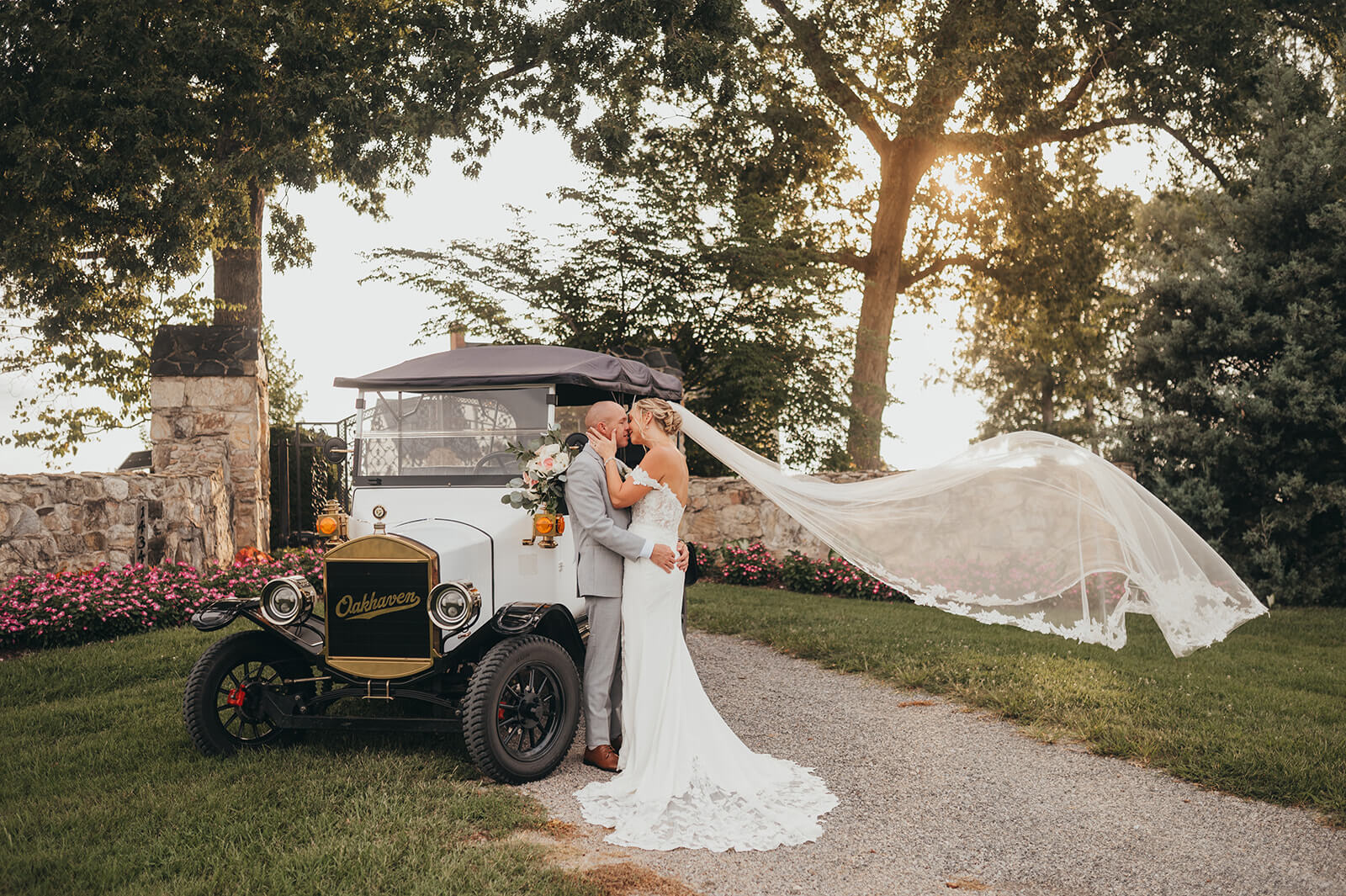 A bride with a long veil blowing in the breeze standing next to Oakhaven's Model T golf cart.