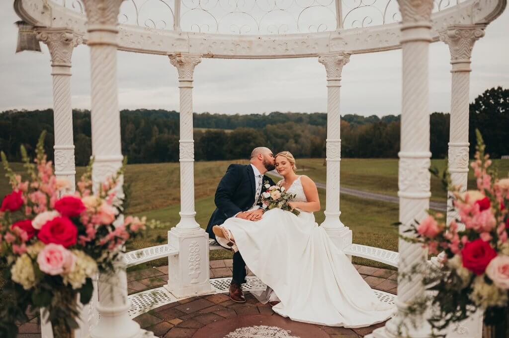 A bride and groom sitting for a portrait inside the wrought iron gazebo at Oakhaven in NC.