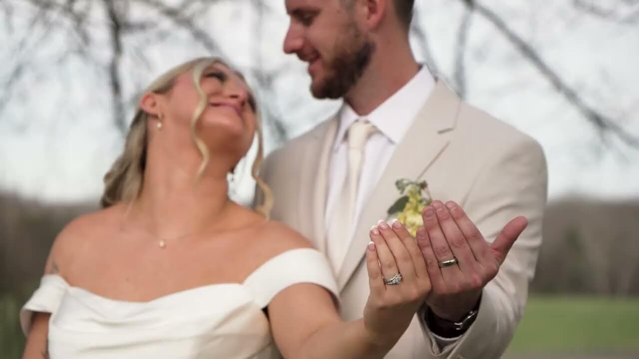 A wedding couple outside, showing off their rings.
